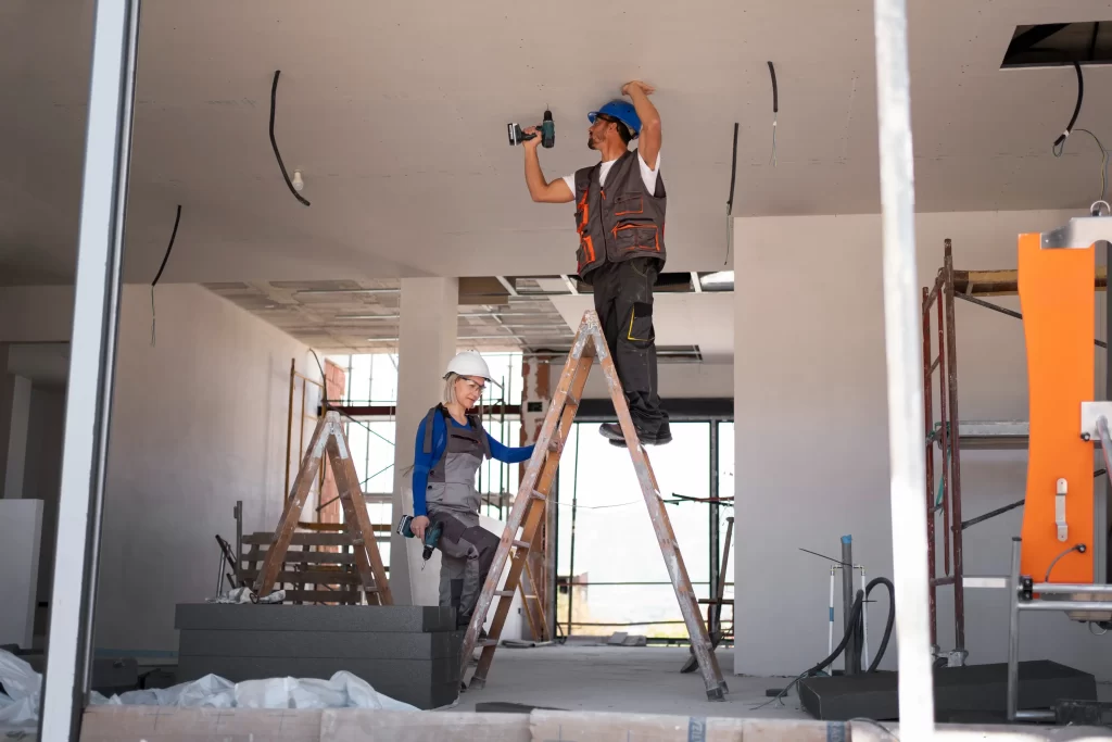 Hombre y mujer de la construcción de pie en escalera reparando