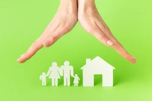 Manos en primer plano, protegiendo figuras de papel que representan una familia y su casa.